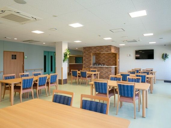 ブルーの椅子がセットされた木製のダイニングテーブルセットが複数置かれた食堂には白い花も飾られている。