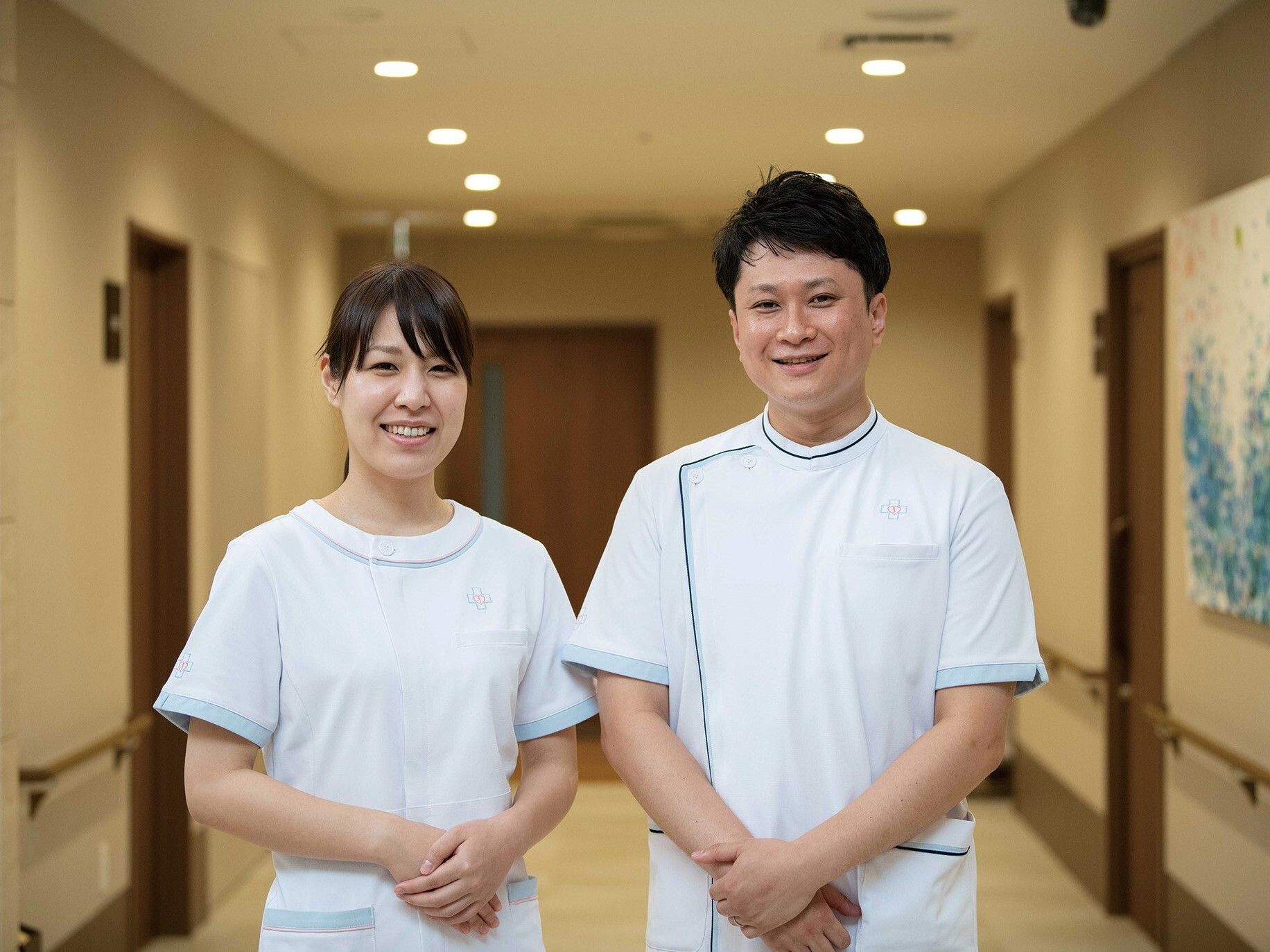 車いすの高齢女性のそばに腰を下ろして手を取り、微笑みかけているエプロンを付けた女性スタッフ。