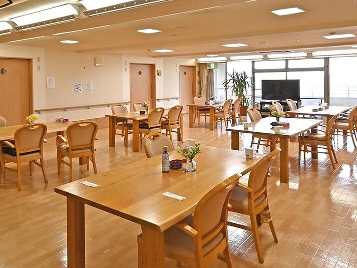四人掛けのテーブルと椅子が並べられている施設内のリビングスペースの様子