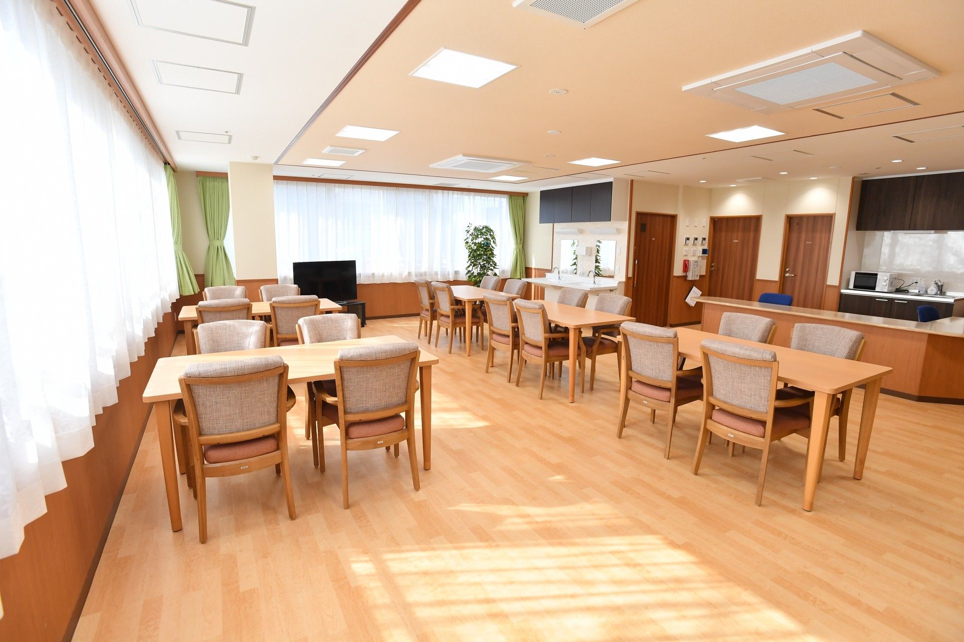 四人掛けのテーブルと椅子が並べられている施設内のリビングスペース