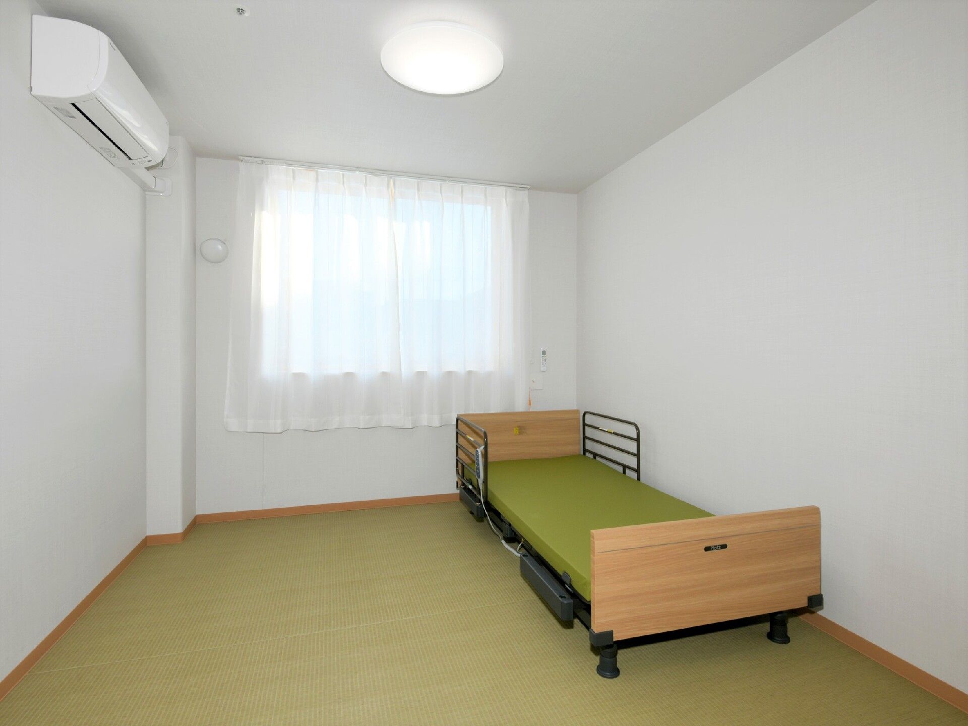畳調の床を敷き、エアコンや介護用ベッドを備えた部屋