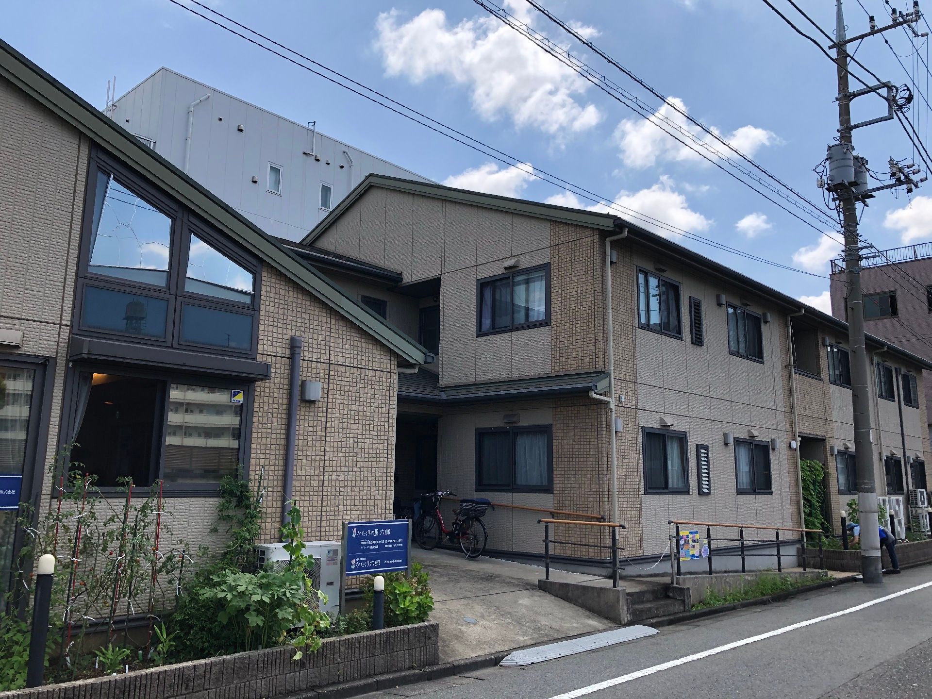 ブラウン系の２階建ての建物は道路に面していて、少し坂になっている。建物の前には手すり付きのスロープがある。