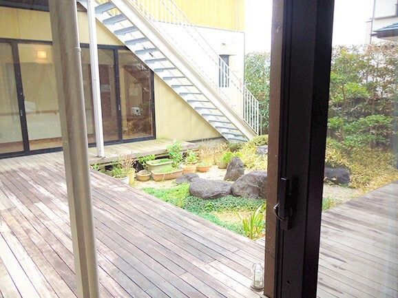 屋外階段が設置され、庭先につながっている。庭を囲むようにしてウッドデッキのテラスが設置され、プランターも置かれている。