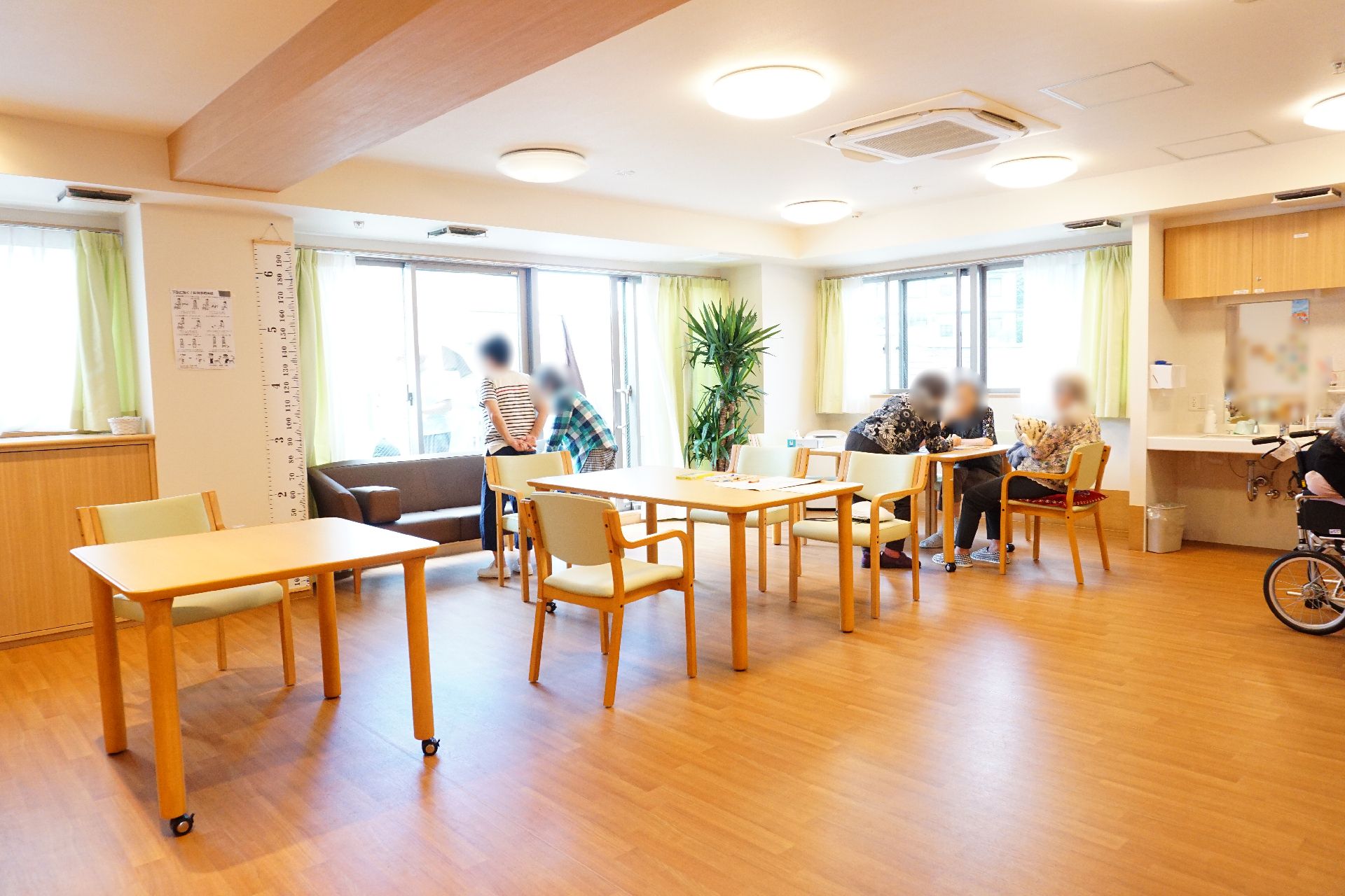 窓が多く設置され、テーブル、椅子が多数置かれているリビング
