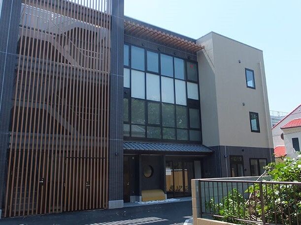 4階建ての建物はブラウン系で、中央部分には大きな窓があり、玄関には屋根がある。