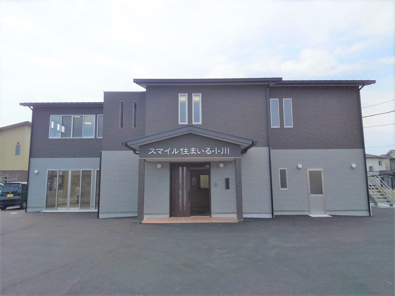 2階建ての建物は２階部分がダークグレー、１階部分がライトグレーで、広い敷地内には車を止めることもできる。玄関の屋根にはホーム名が書かれている。