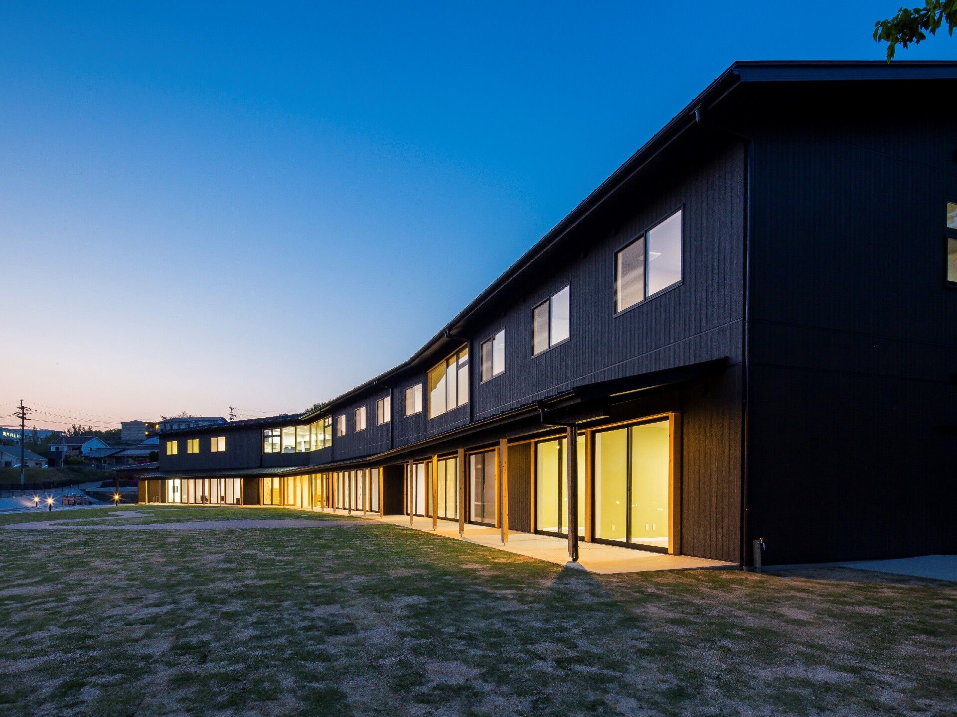 薄暗くなりライトアップされた建物。窓が多く、建物全体がライトアップされ、広い庭園も付いている。