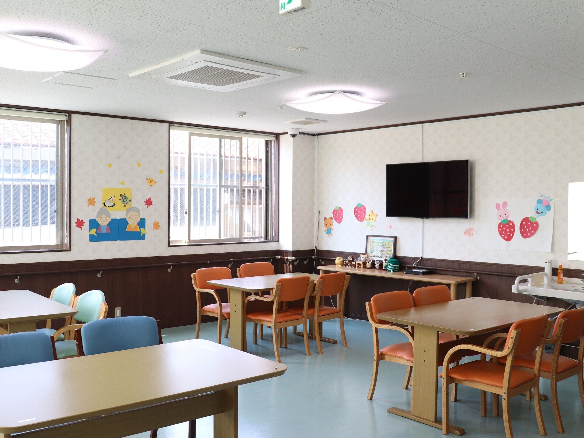 木製のダイニングテーブルが複数置かれ、ぬくもりが感じられる明るい食堂。手作りの飾りも壁に飾られている。