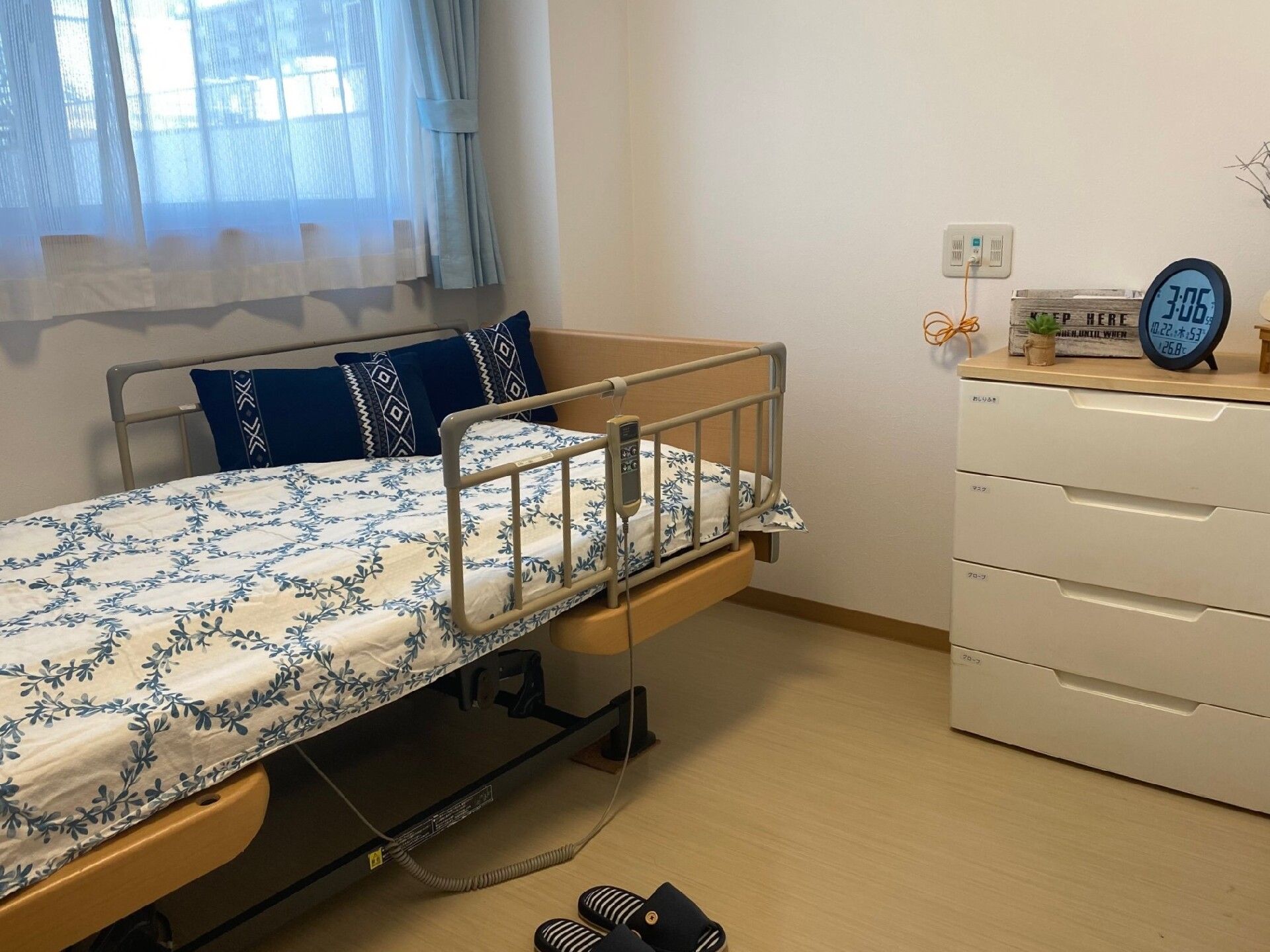 寝具付きのベッドやタンスが置かれた居室。ベッドのそばには緊急通報装置があり、時計などの小物も持ち込まれている。