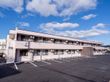 白っぽい外壁の２階建ての建物は日当たりのいい場所に建っている。広い駐車場も付いている。