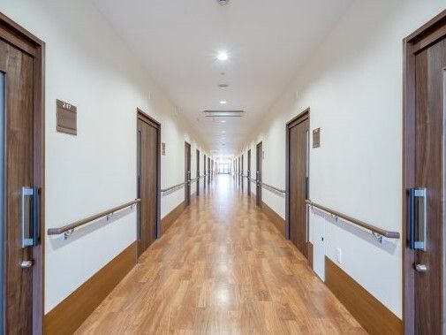 両サイドに手すりと居室のドアがあり、まっすぐな廊下の突き当りには窓があり、明るい。