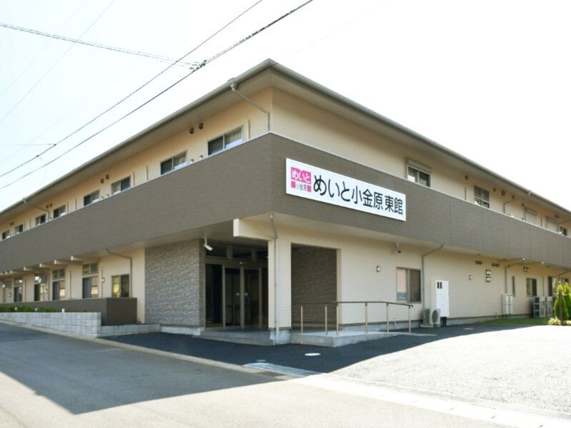 2階建ての建物はベージュ系でブラウンの屋根とベランダが付いている。玄関先に手すり付きのスロープがあり、ホーム名が外壁に書かれている。