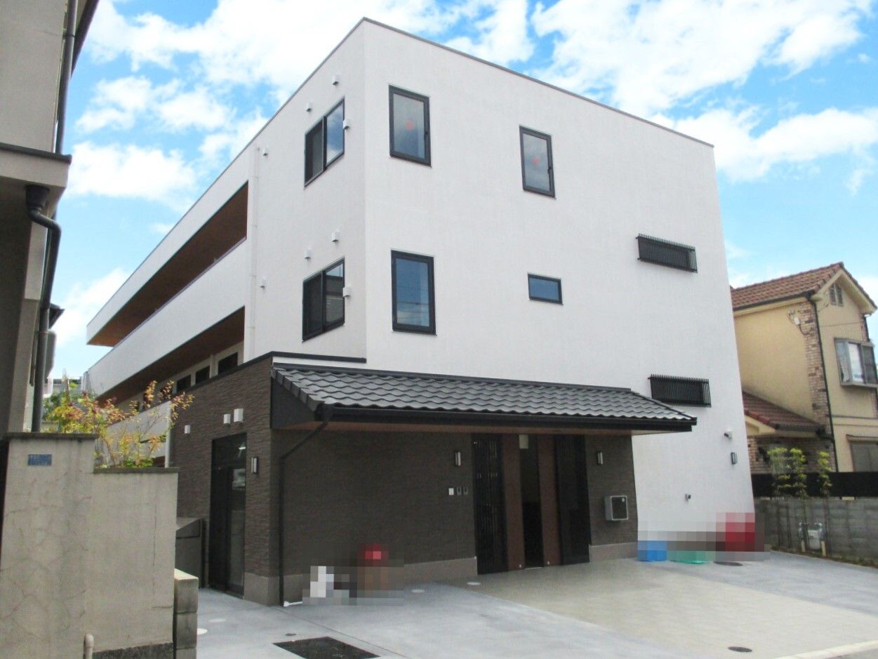 3階建ての建物は白をメインとしていて、1階部分がブラウン。2階と3階にはベランダが付いている。