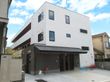 3階建ての建物は白をメインとしていて、1階部分がブラウン。2階と3階にはベランダが付いている。