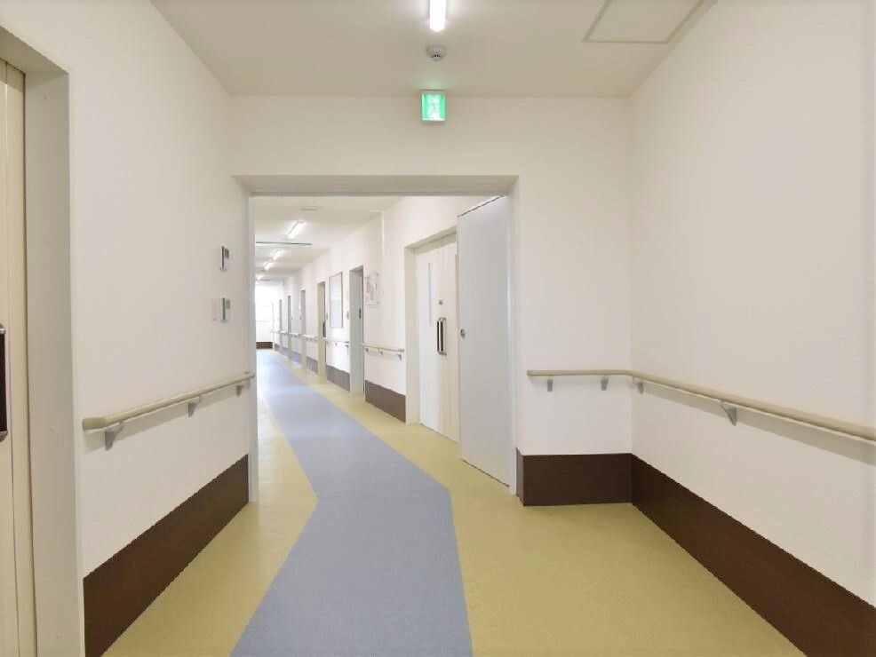 手すりと居室のドアが両サイドに付いた廊下。日当たりがよく、フロアは中央がブルー、再度が黄色と色分けがされている。