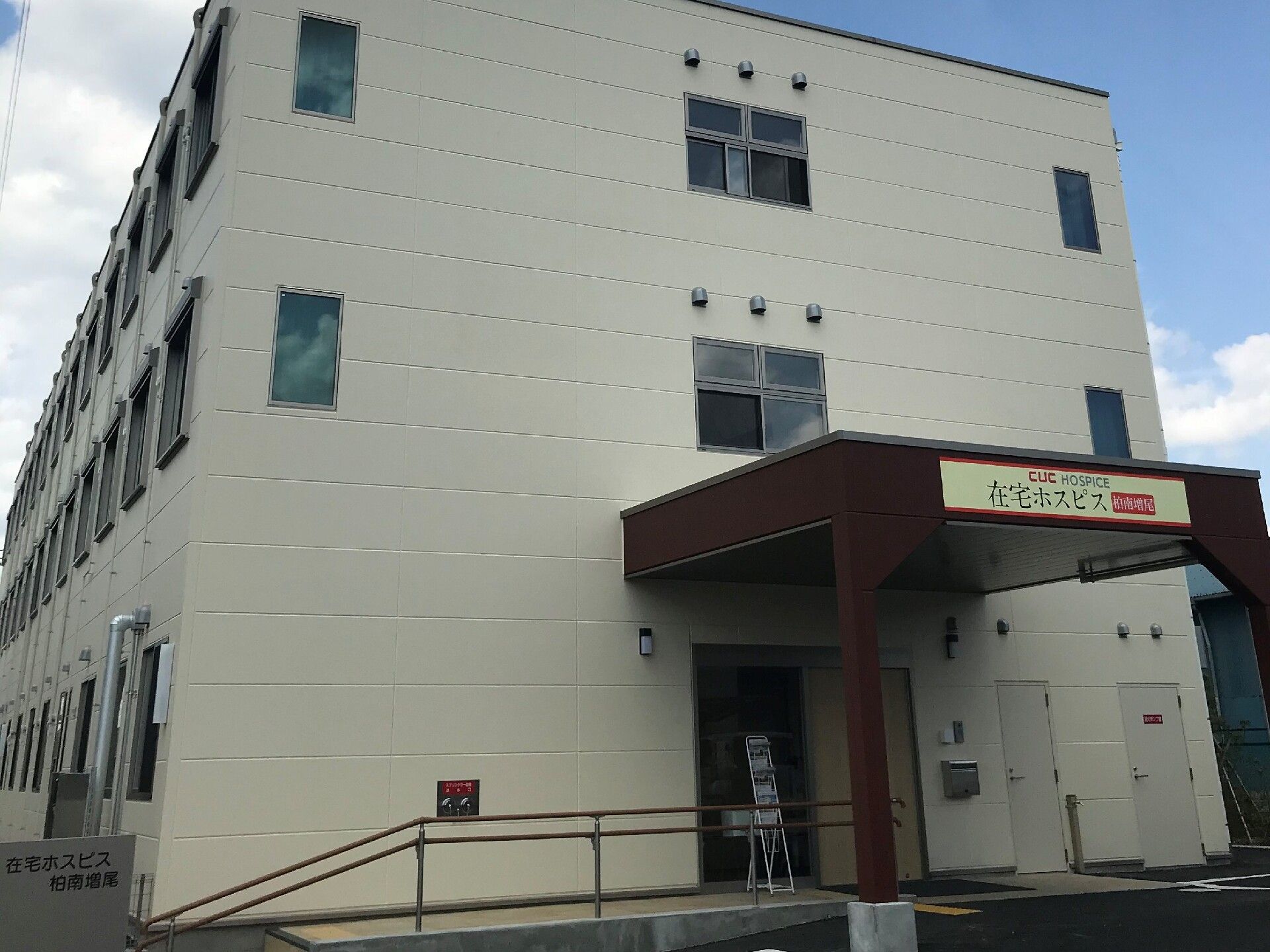 駐車場が付いた３階建ての建物は白を基調としていて、玄関先には屋根が付いている。