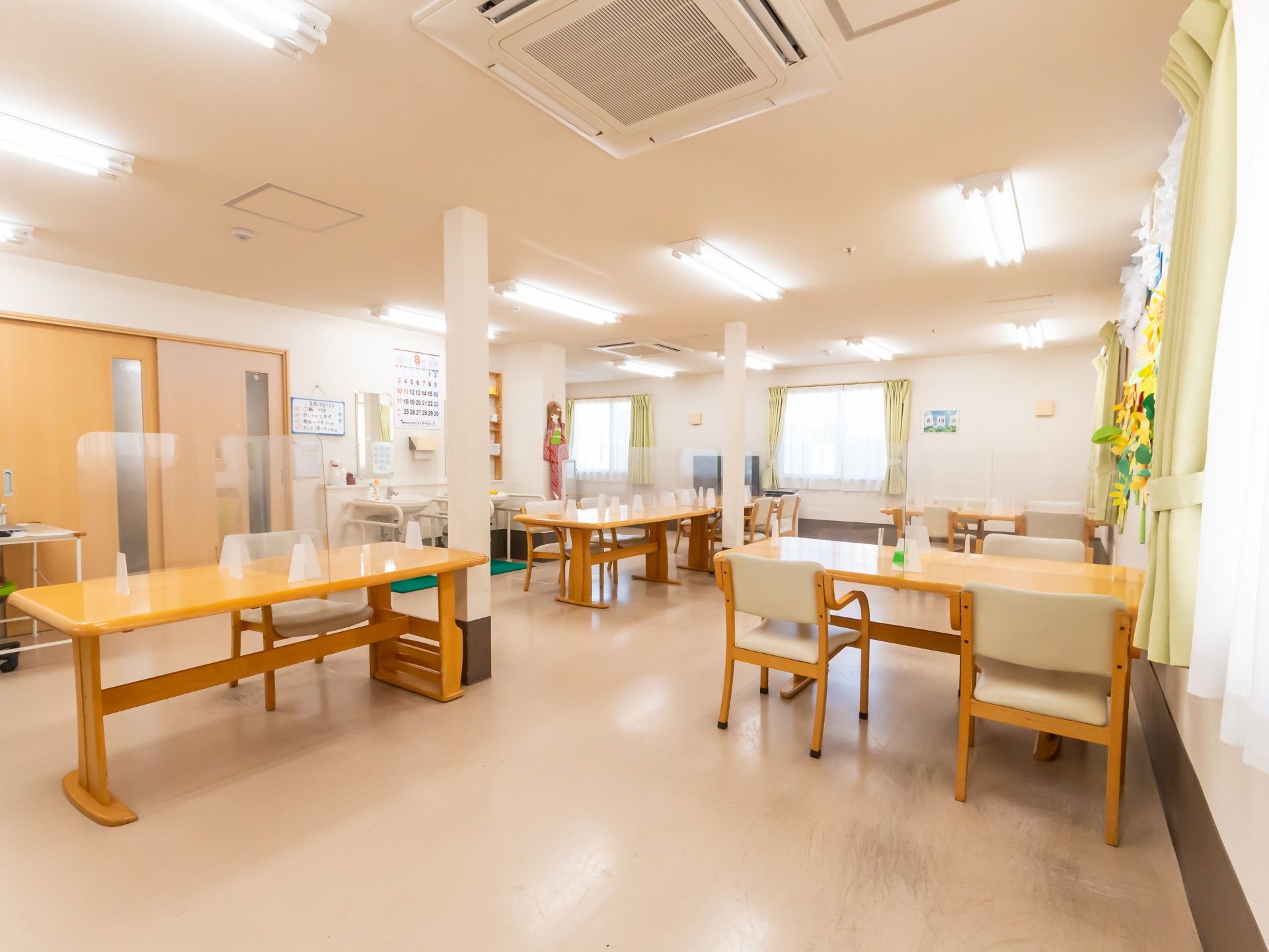 緑の多い屋外で笑顔で散歩を楽しんでいる車いすの高齢女性とエプロンを付けた女性スタッフ。