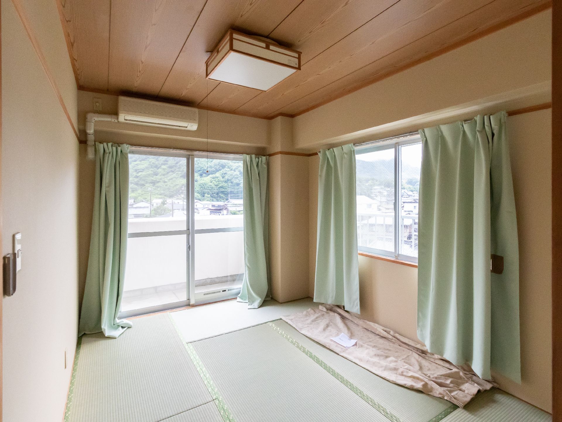 壁の２面に緑のカーテンが付いた大きな窓ガラスがある畳が敷かれた部屋