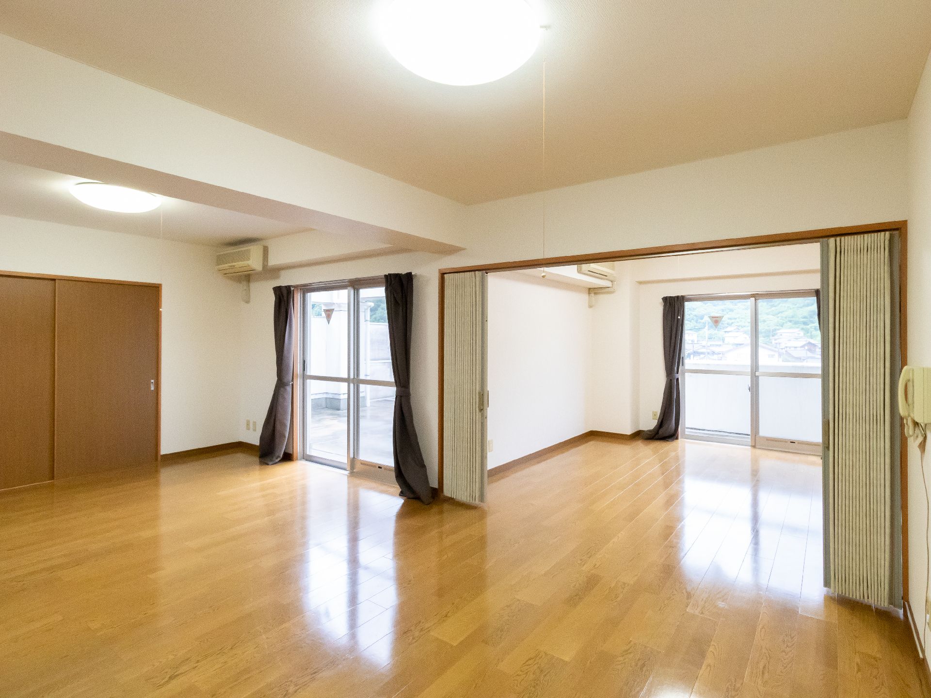 大きな窓がある広々とした何も置かれていない白い壁でフローリングの床の部屋