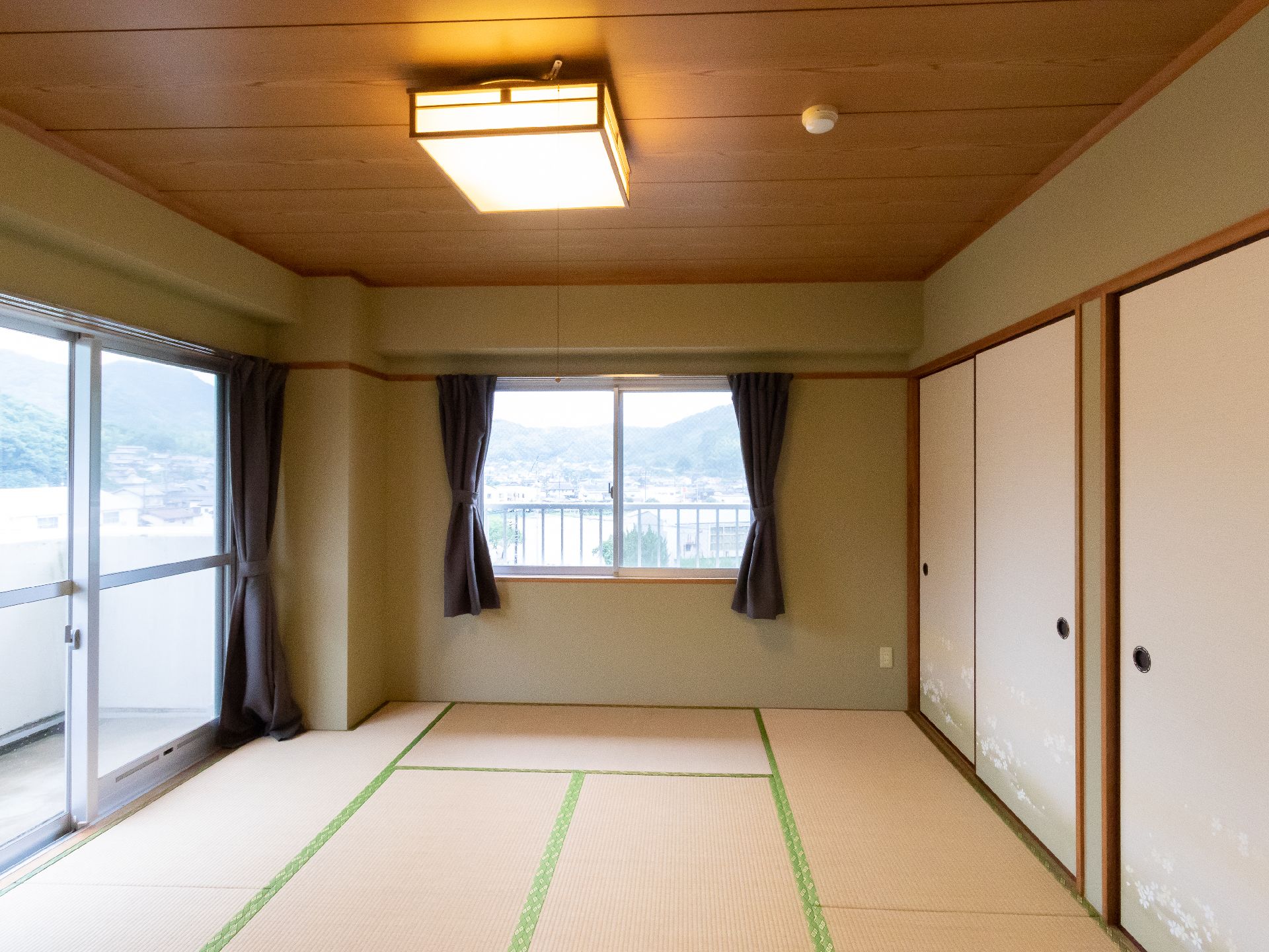壁の２面にカーテンのついた窓が配置されている畳が敷かれた部屋