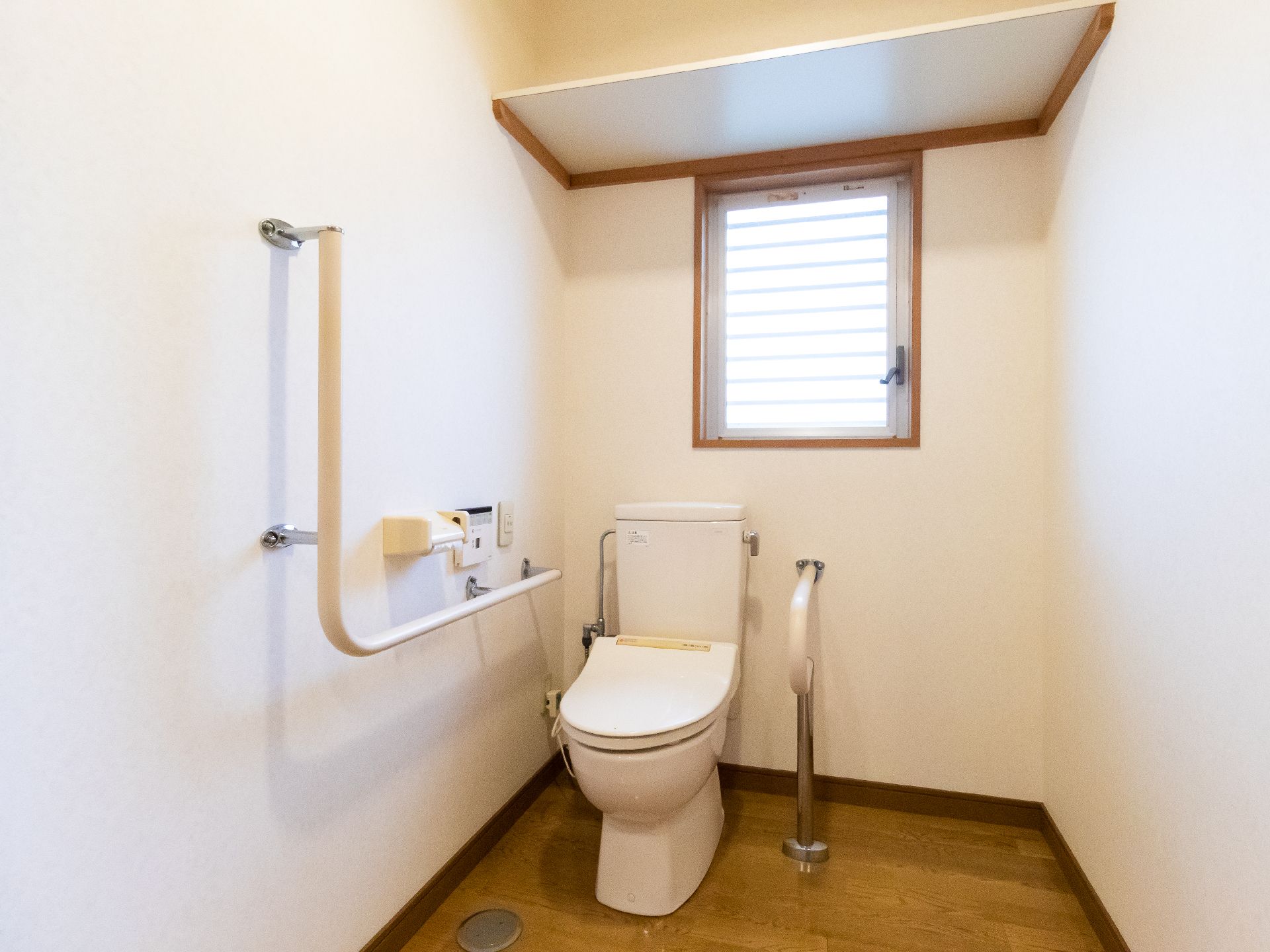 手すりに囲まれた白い洋式便器が置かれた窓がある白い壁の部屋