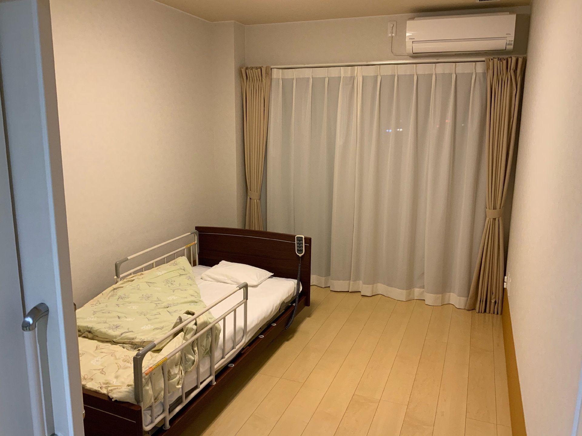 フローリングの居室。カーテン付きの窓とエアコン、ベッドがあり、寝具もついている。