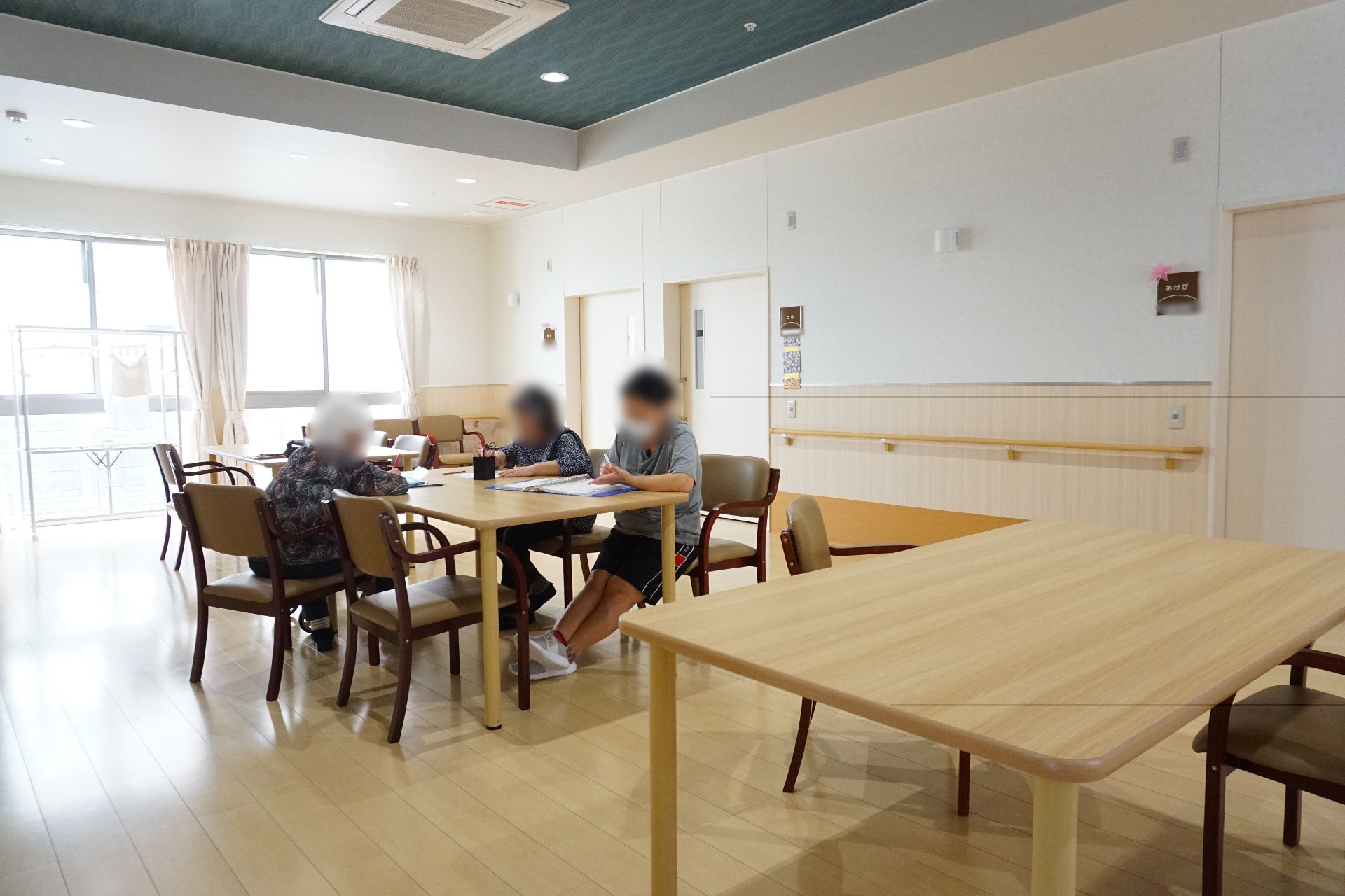 窓から陽光が入り、複数のテーブルが置かれているリビング