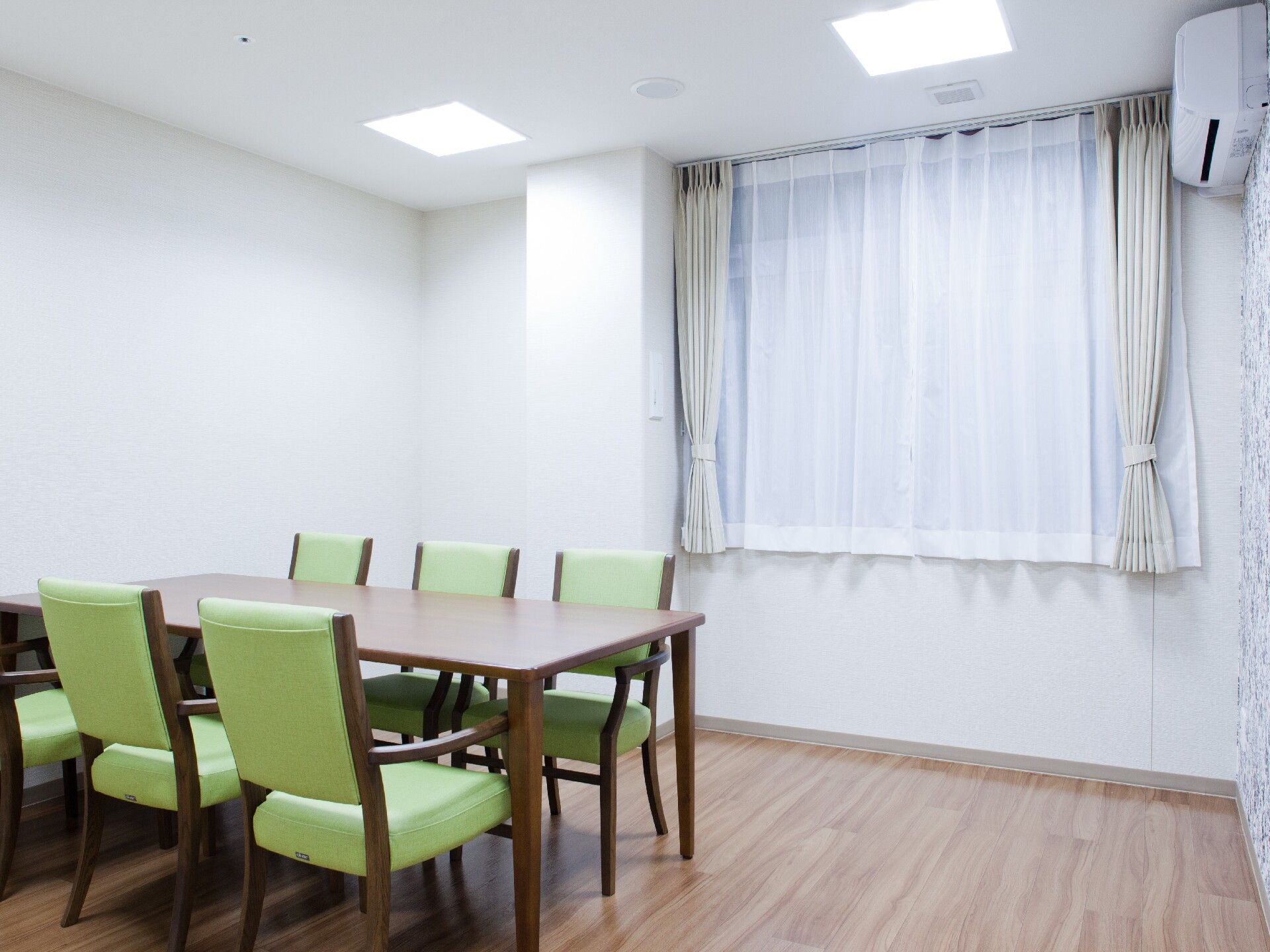 6人掛けのテーブルがセットされたフローリングの部屋にはエアコンが付き、大きな窓にはカーテンもある。