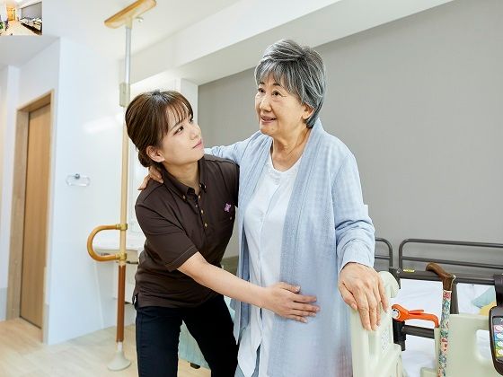 キッチン付きのフローリングの部屋の壁にはオレンジの緊急通報装置とピクチャーレールが設置されている。
