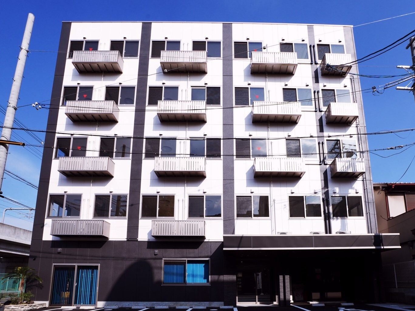 白をメインとした5階建ての建物には車寄せやベランダが付き、周辺にも建物がある。