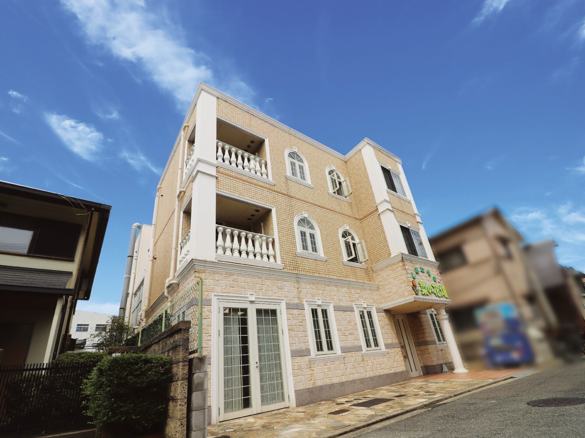 3階建ての建物はベージュ系で玄関の屋根部分にはホーム名が書かれている。2階と3階にはテラスも付いている。
