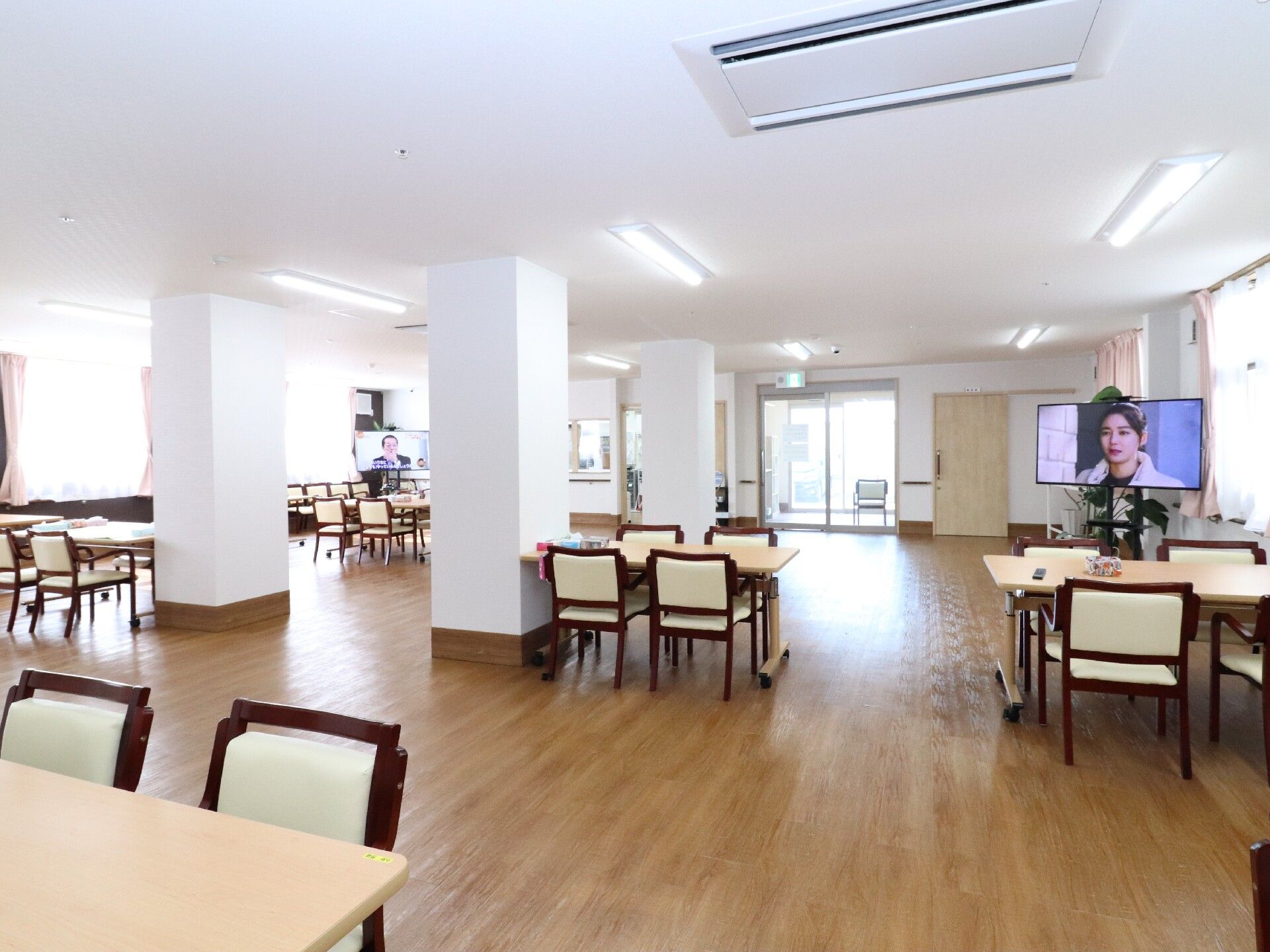 4人掛けのダイニングテーブルがゆったりとした配置で並び、奥にはテレビも設置された明るい雰囲気の食堂。