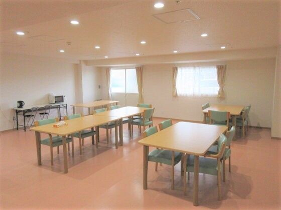 大きな窓が付いた明るい食堂には木製の大きなダイニングテーブルが複数置かれ、壁際のテーブルには電子レンジなども置かれている。