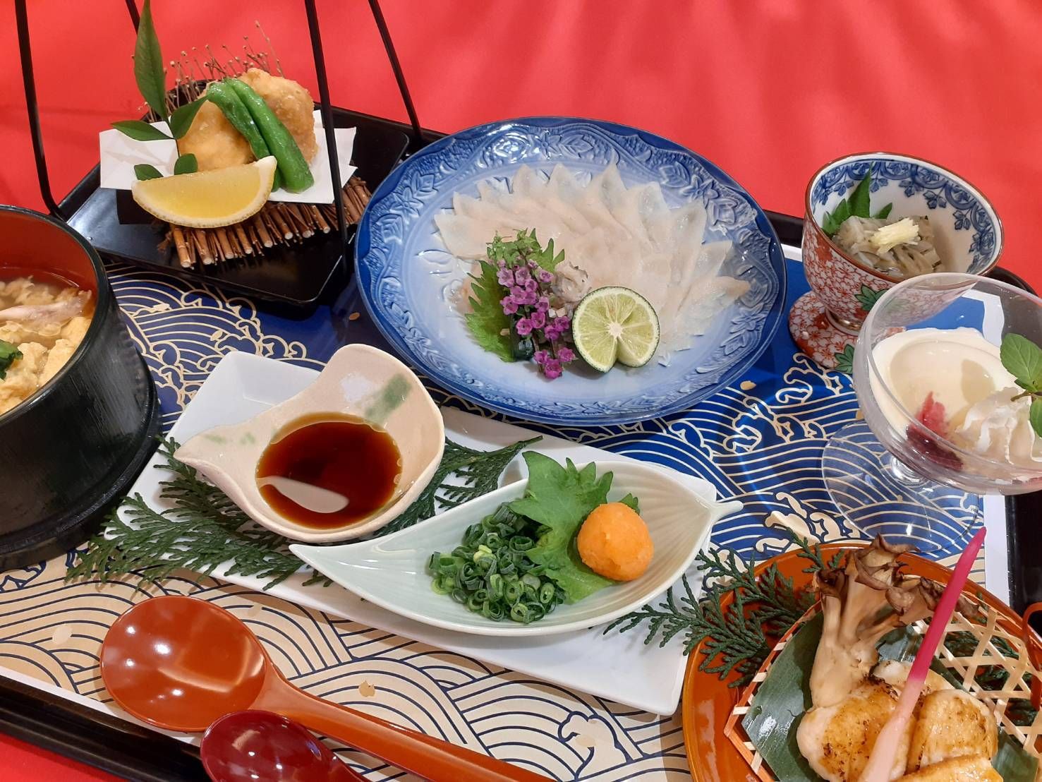 ふぐ刺しや揚げ物、しょうがが添えられた焼き物、前菜やデザートが添えられた食事。