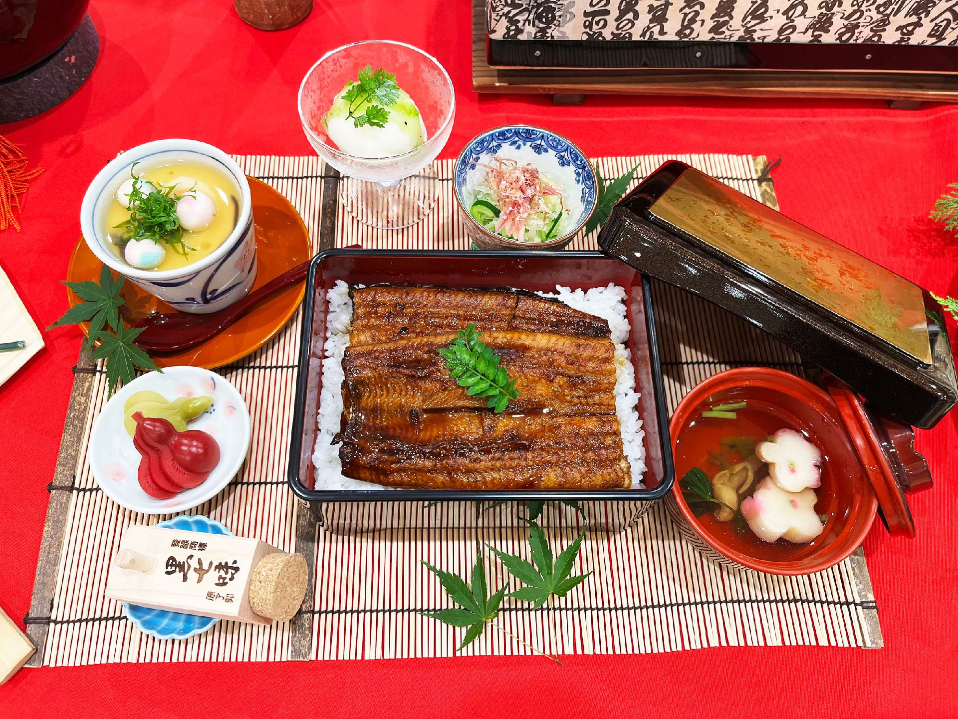 山椒の葉が添えられたうな重をメインに吸い物や漬物、デザートなどが並べられ、青い紅葉が飾られている。