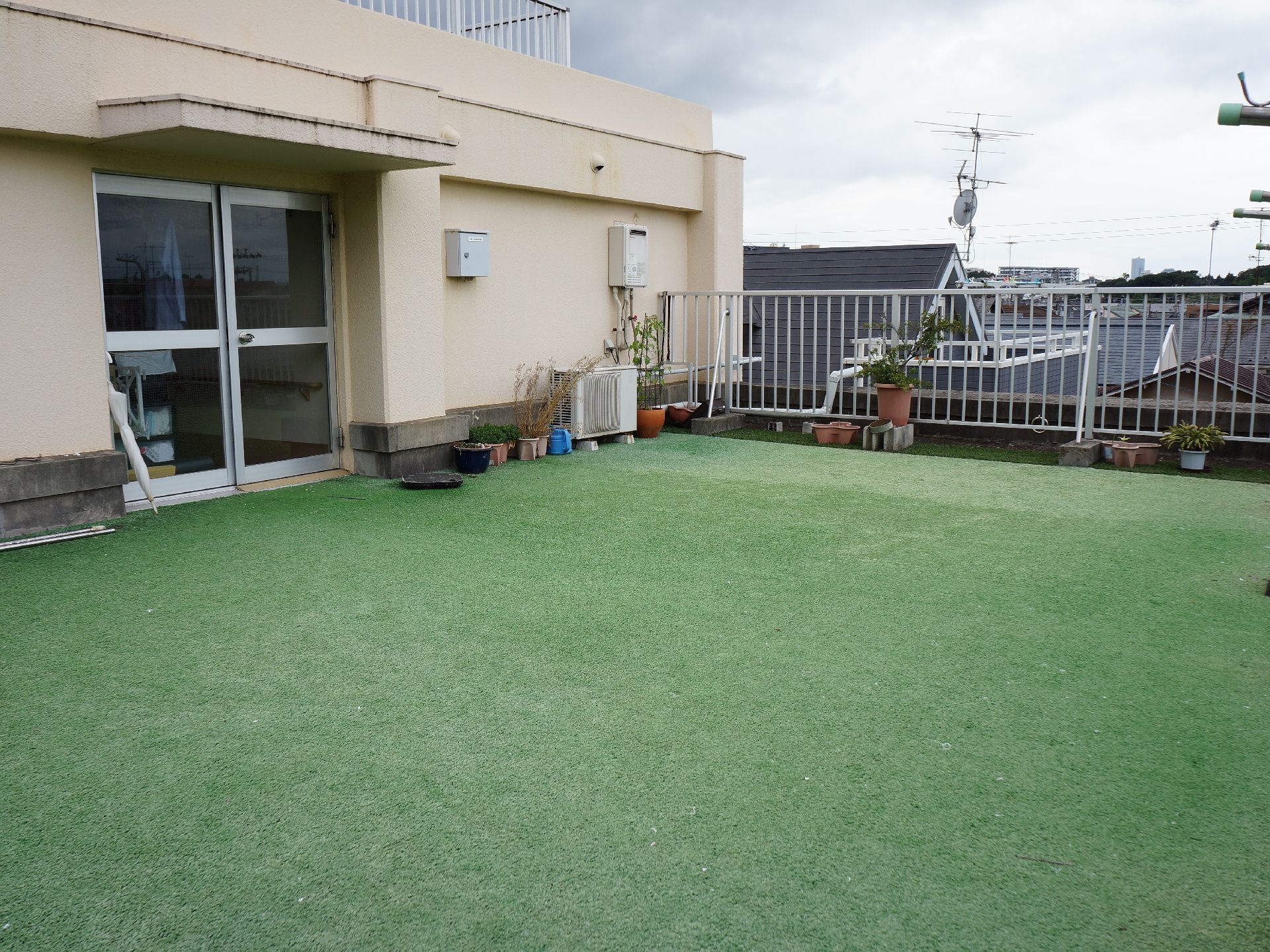 テラスの様子を写したもの。床には人工芝が全面的に敷かれている。縁には柵がせっちされていて、物干し台が置かれている。
