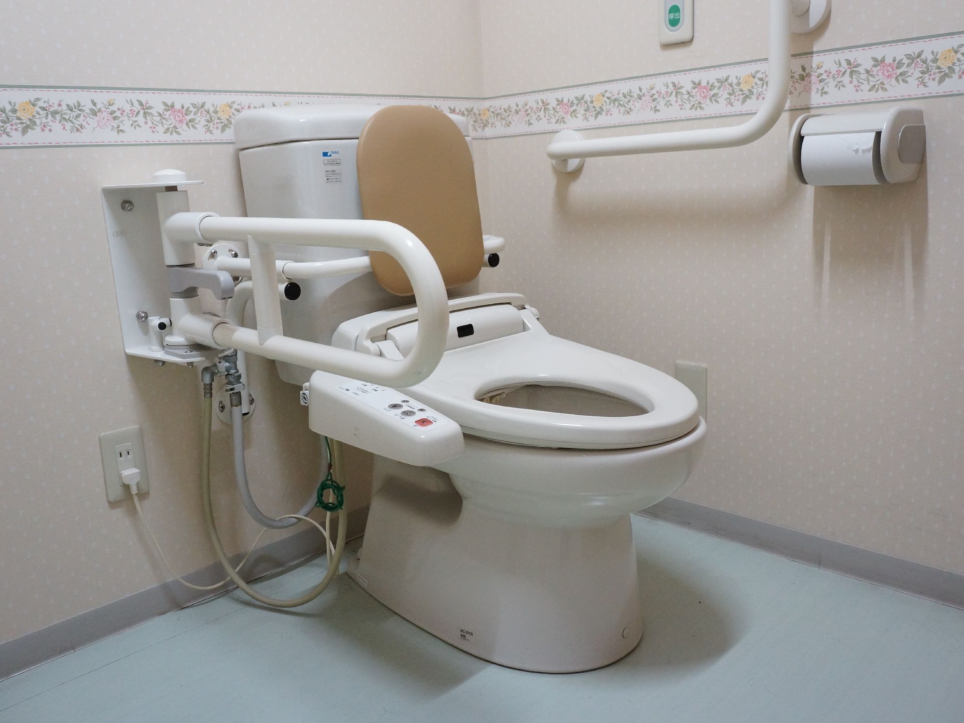 温水洗浄機能付きの洋式トイレ。背当てが付いている。手すりも付いていて、便座の右側のものは可動式になっている。