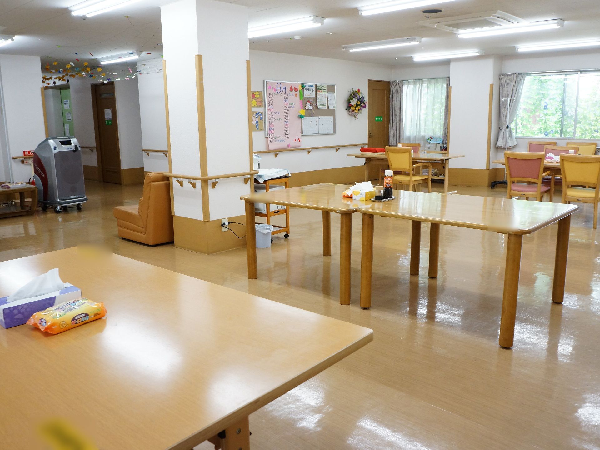 食堂・談話室の中央辺り。大きな木のテーブルが2台、横にくっつけて並べてある。椅子は1脚もセットされていない。