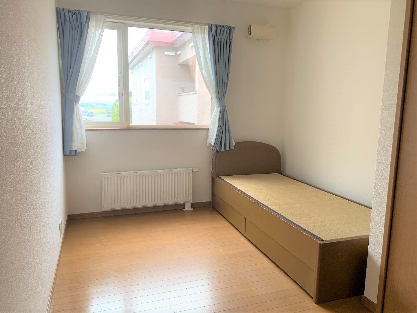シンプルなベッドが置かれたフローリングの部屋にはカーテンが付いた窓があり、外の景色を見ることができる。パネルヒーターも付いている。