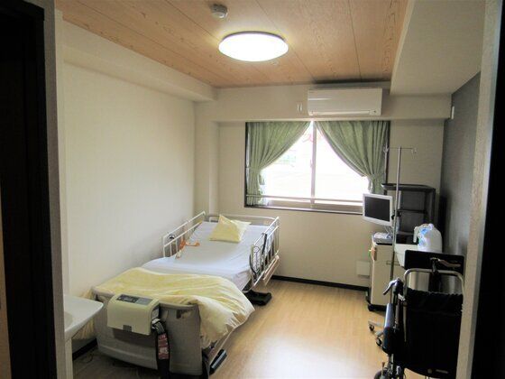 エアコン付きのフローリングの個室にはカーテンが付いた窓と、介護用ベッドが置かれ、テレビやデスクセットもついている。