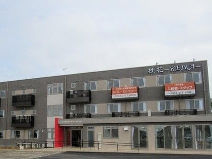 ３階建ての建物はベージュとブラウン系で玄関部分には屋根が付き、手すり付きのスロープも付いている。