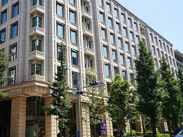 緑に囲まれた大きな建物は窓が多く、歴史を感じられる外観。青空が広がっている。