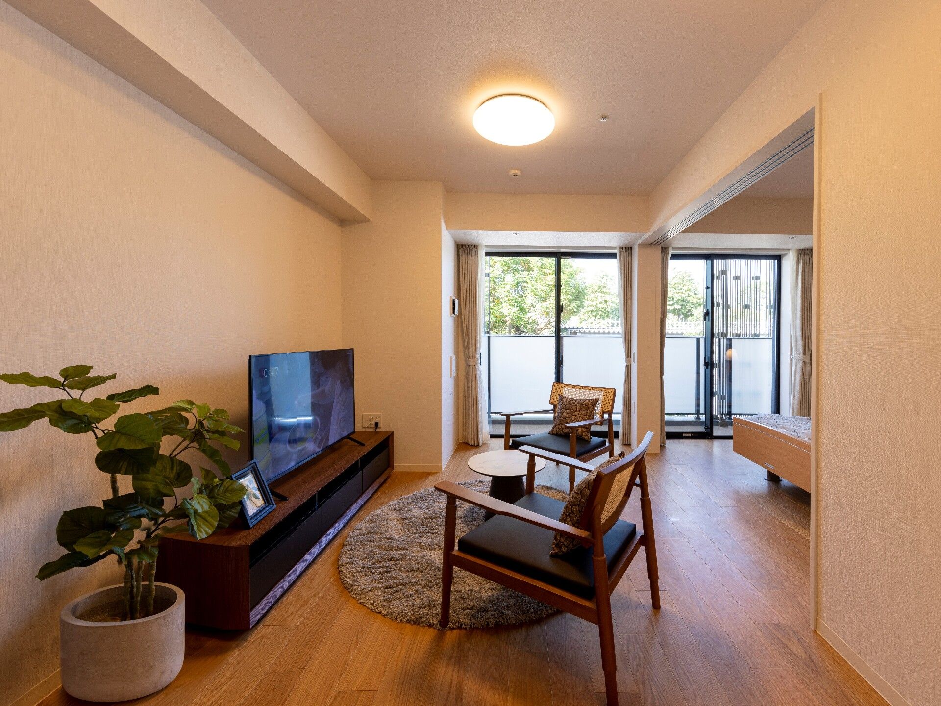 テレビやテーブルセット、観葉植物が置かれたフローリングの部屋。大きな窓も付いている。