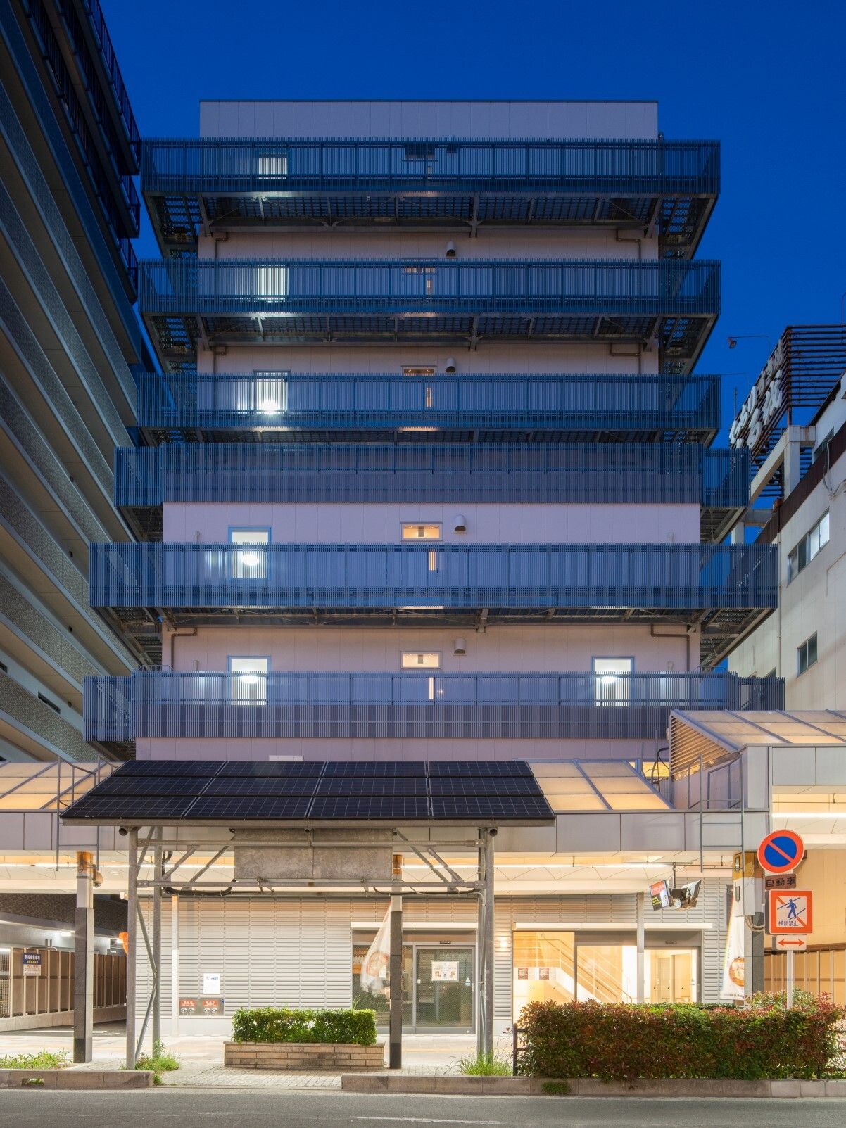 グレーの8階建ての建物は街中にあり、周辺にもビルがたくさんある。敷地内には緑も植えられ、ベランダも付いている。