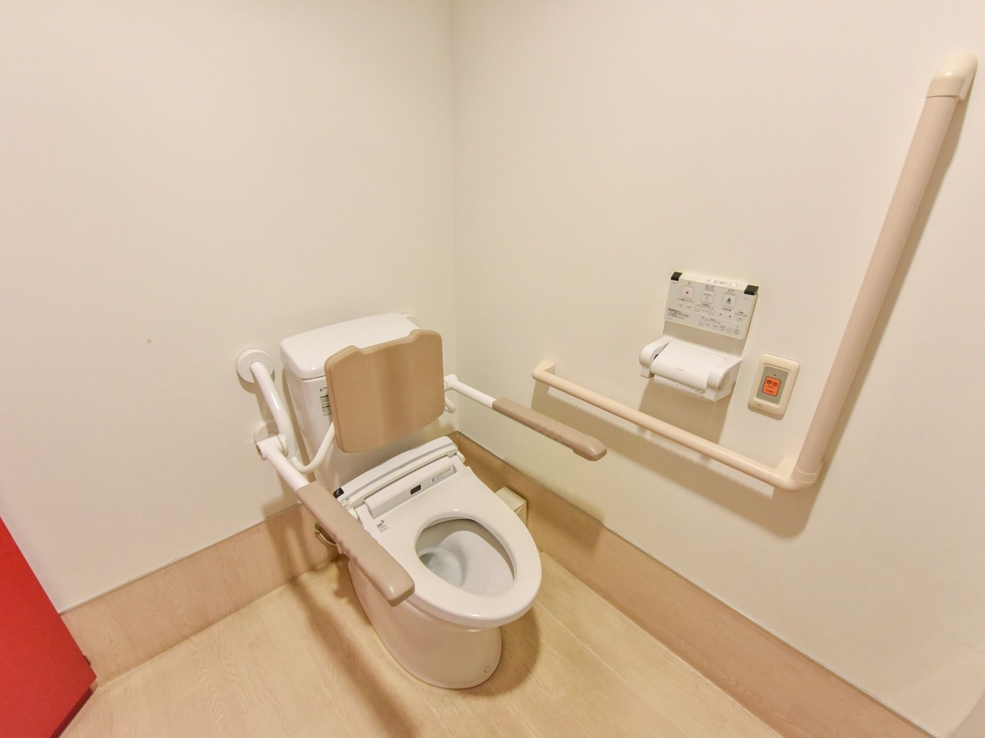 背当てや手すりのついた便器を備えたトイレである。壁には温水洗浄便座のリモコンやナースコールが設置されている。