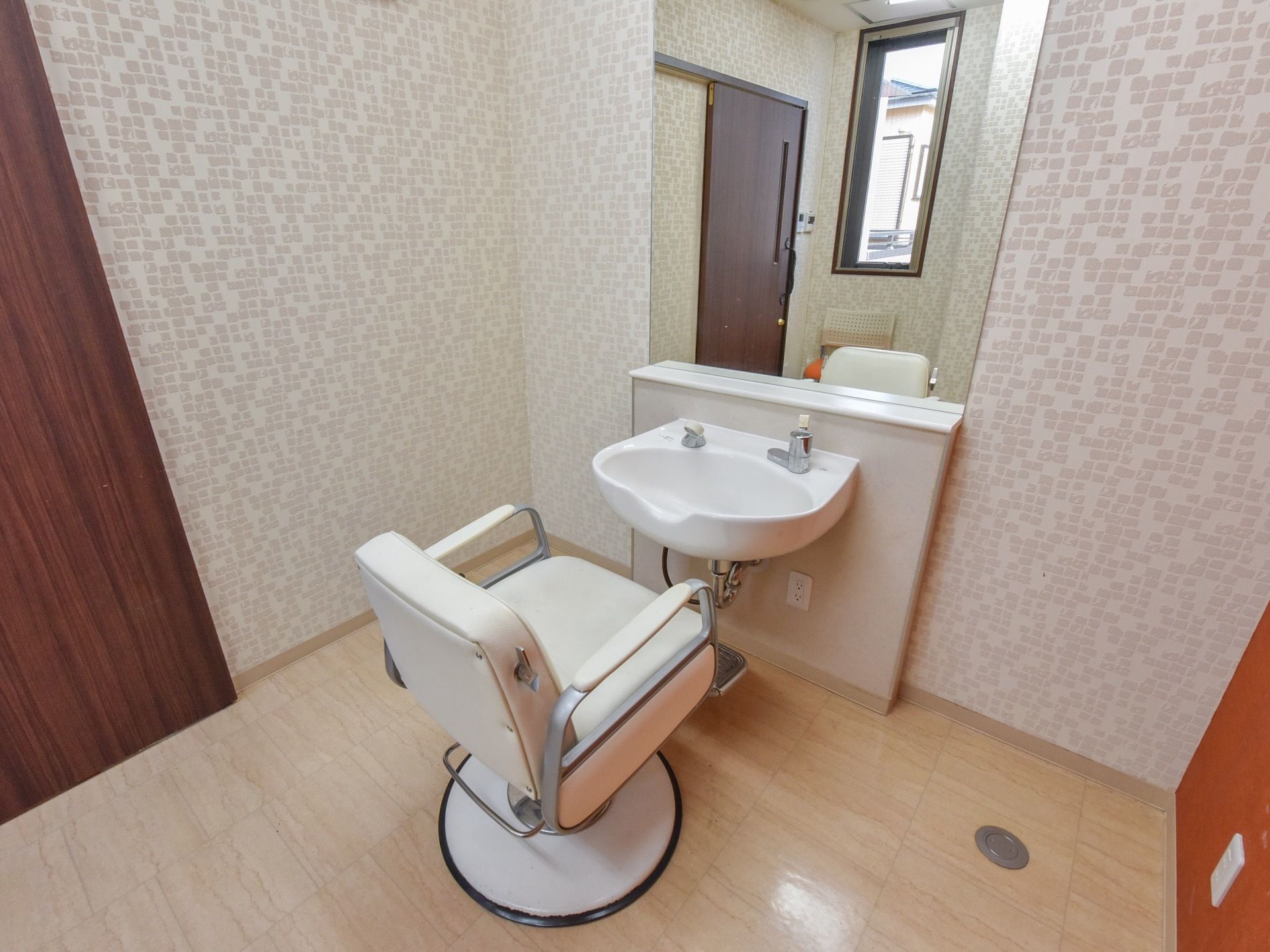 大きな鏡の前に、くぼみのある洗面台が置かれている。その前に、アイボリー色の革の貼られた椅子がある。下にペダルがついている。