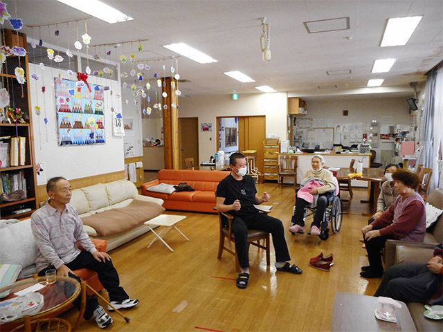 椅子に座ったスタッフが中心としてその周りに入居者が座り、レクリエーションを行っている様子。