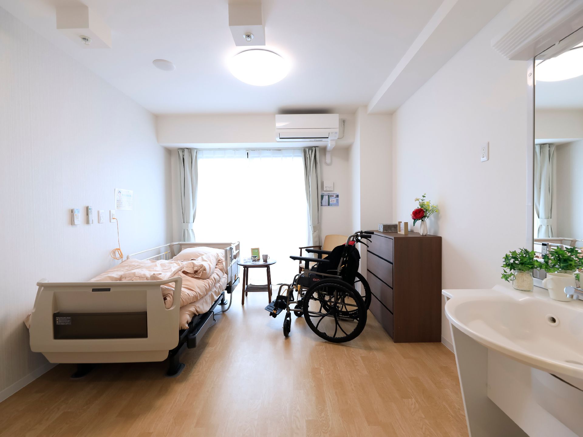 大きな窓があり、介護ベッドや家具に光が降り注いでいる居室
