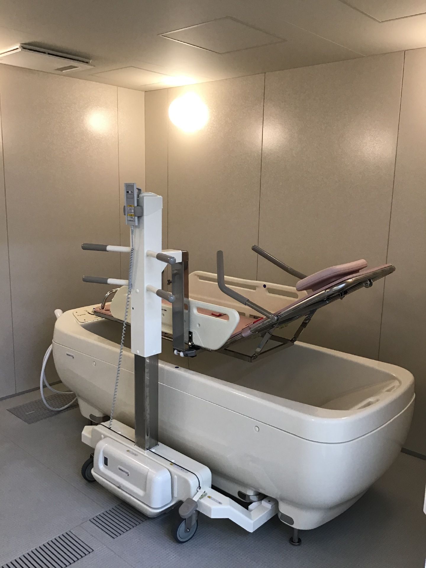寝たまま入浴できる寝台浴を設置した浴室。照明が付きストレッチャータイプのリフトが付いた浴槽のような機械がある。
