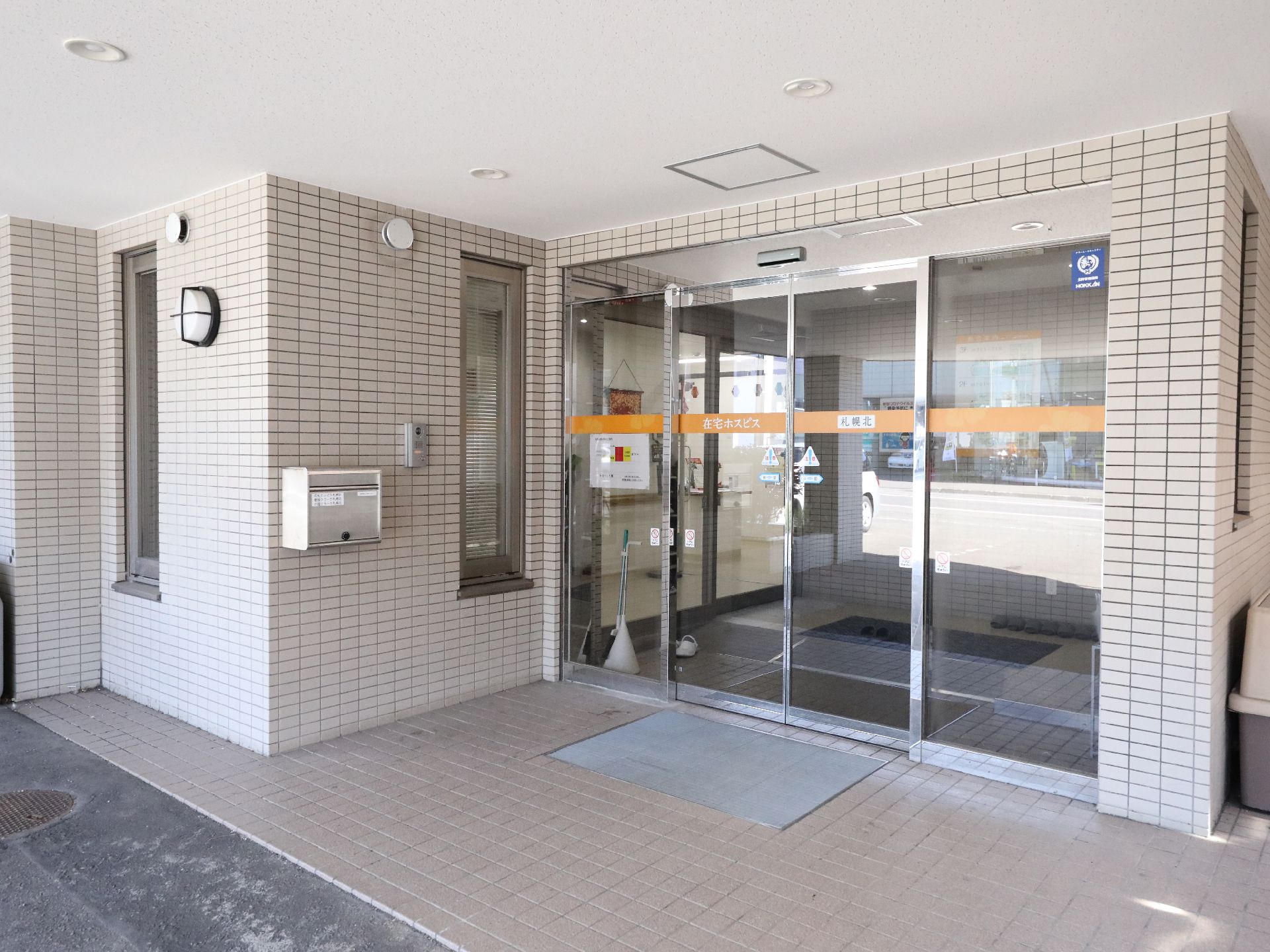 日当たりのいい共有スペースで黄色のカーディガンを着た高齢女性にエプロンを付けた女性スタッフが寄り添っている様子。